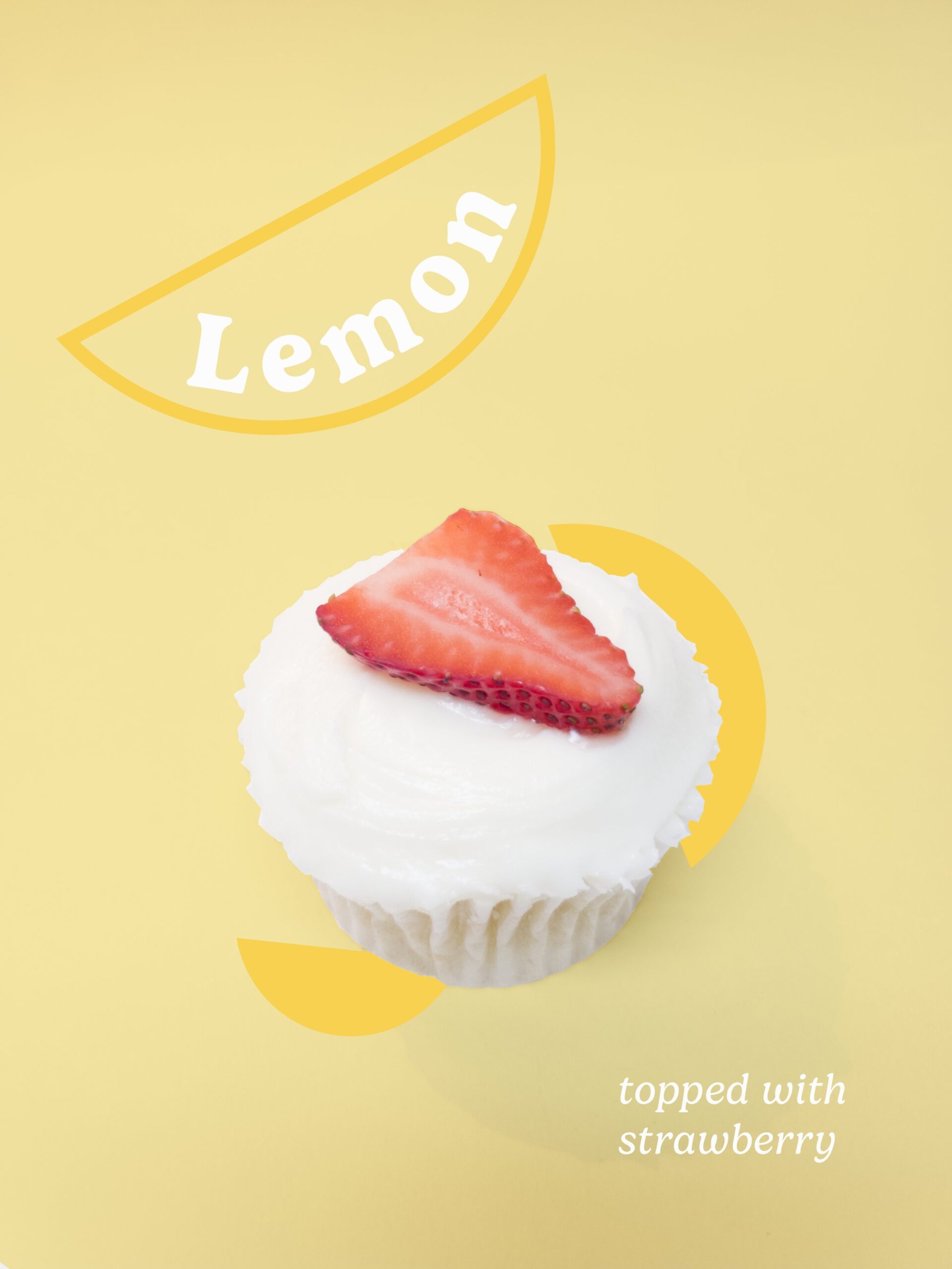 Photograph of a lemon cupcake with a strawberry slice on top on a light yellow background